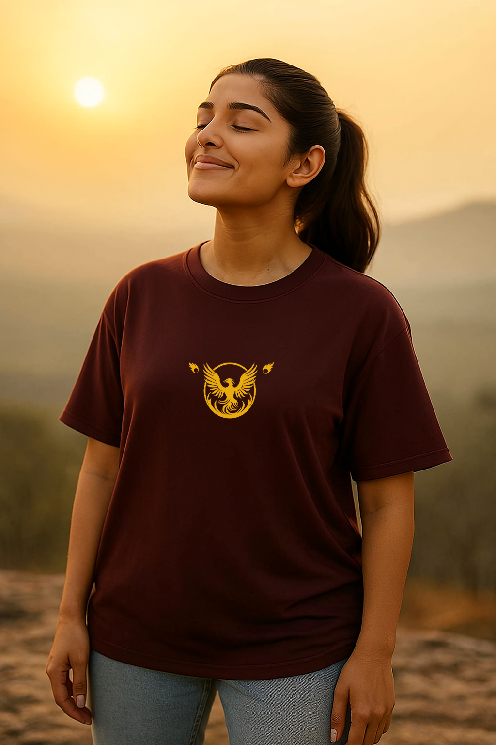 Woman wearing a maroon t-shirt with a yellow logo against a sunset background