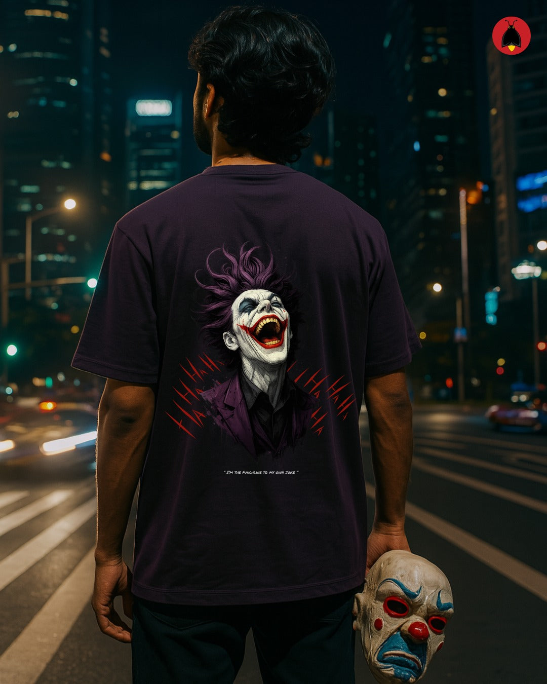 Person wearing a dark t-shirt with a Joker graphic on a city street at night.