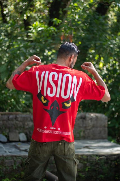 Person wearing a red 'VISION' t-shirt with a graphic design outdoors.