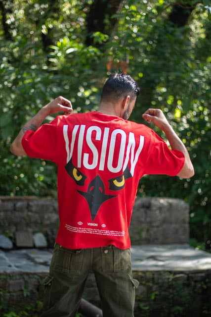 Person wearing a red 'VISION' t-shirt with a graphic design outdoors.