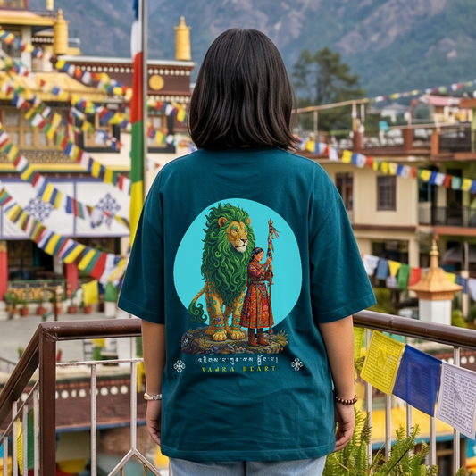 Person wearing a teal t-shirt with a lion and person graphic in front of a colorful building and mountainous background.