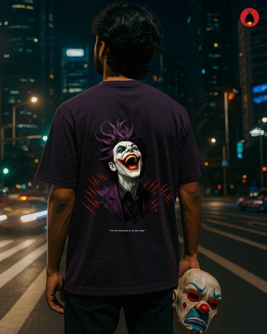 Person wearing a dark t-shirt with a Joker graphic on a city street at night.